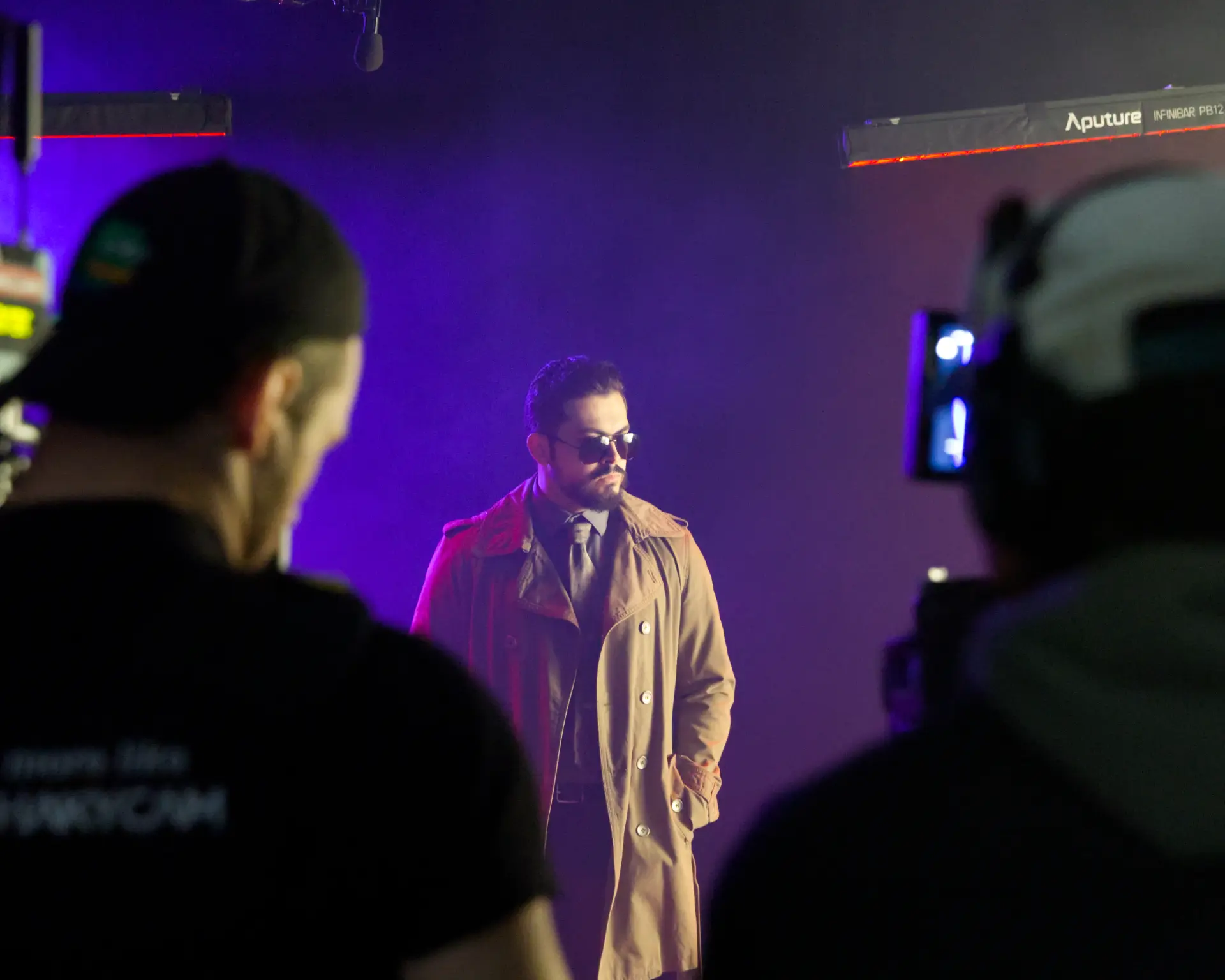 Actor in a trench coat lit in purple on set